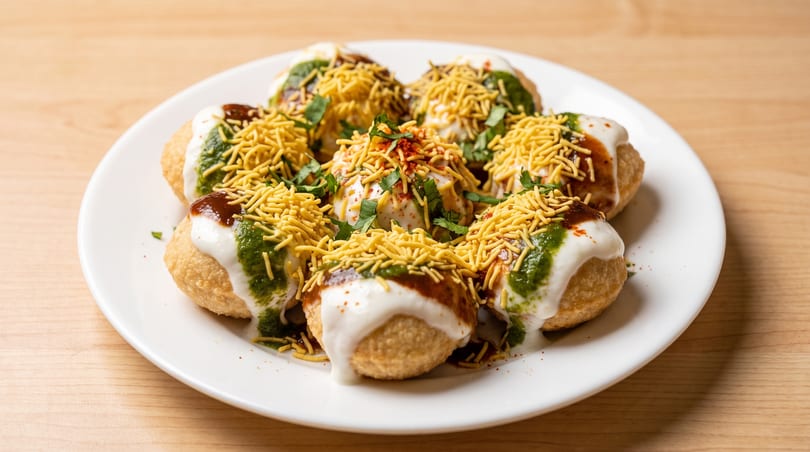 A white plate holds several dahi puri, topped with yogurt, chutneys, and sev.